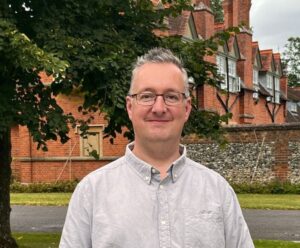 Photo of John Milne with trees and a building in the background.