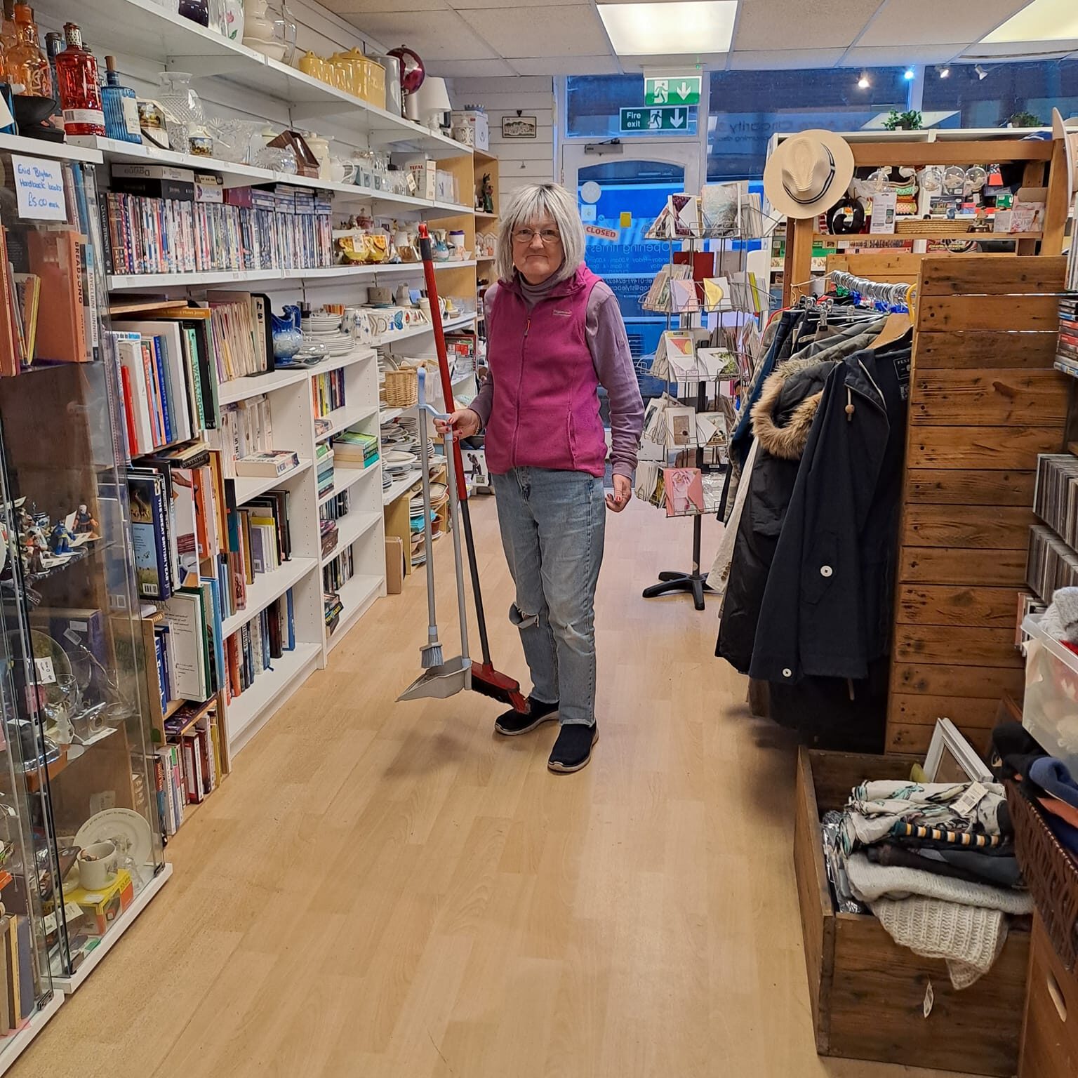 A lady holding a broom and dustpan at the Style Acre Charity Shop
