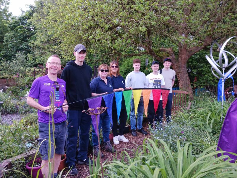 7 Newbury Building Society volunteers standing in Wantage Market Garden holding a rainbow coloured flag