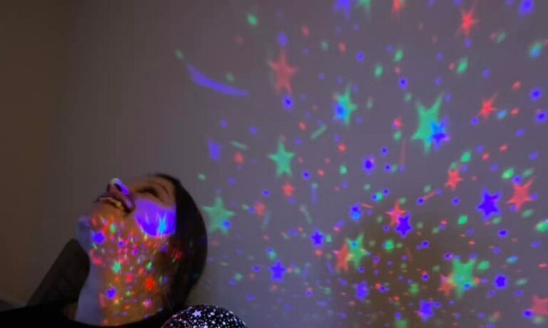 Person smiling looking upwards at lights projected on wall and ceiling - POP sensory meet ups starting in March