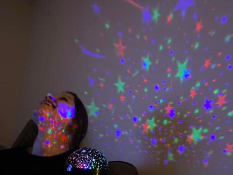 Person smiling looking upwards at lights projected on wall and ceiling - POP sensory meet ups starting in March