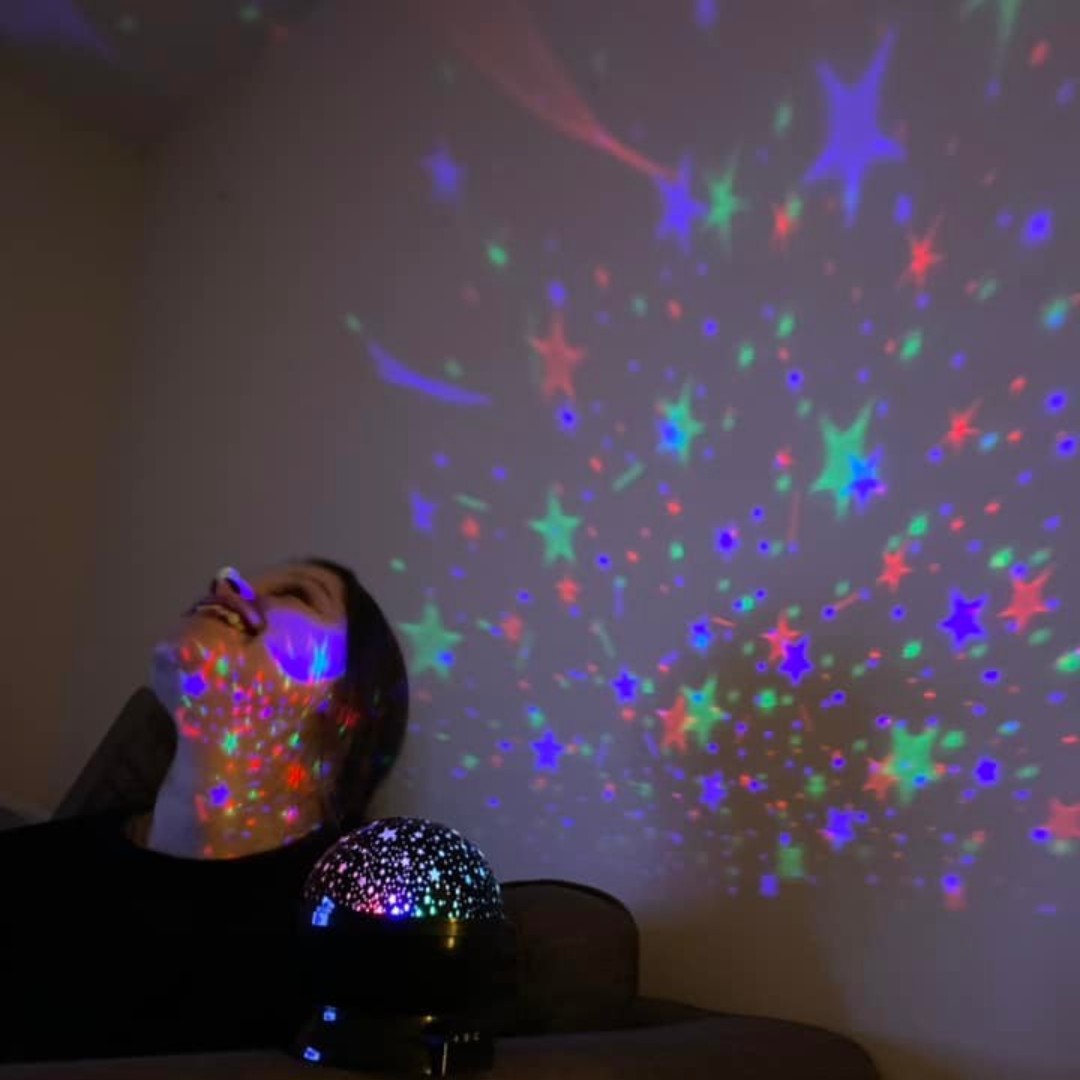 Person smiling looking upwards at lights projected on wall and ceiling - POP sensory meet ups starting in March