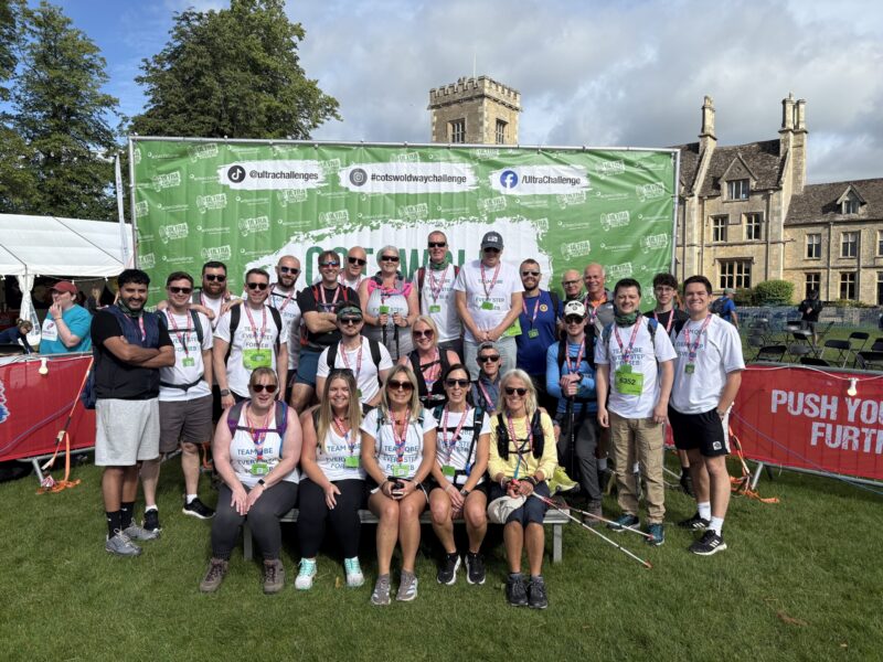 A group of 22 men and women stanging infront of a Cotswold Way Ultra Challenge Sign.