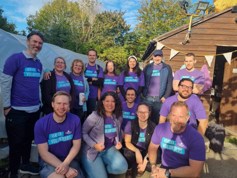 A group photo of 14 people from Vertex standing and kneeling in the wantage market garden